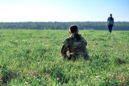 a green field on a summer day sits a man from whom a woman leaves in the distance. divorce couple in the fieldの写真素材