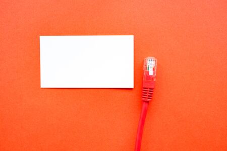 on a red background of paper is an empty business card and an Internet cable with a connector....