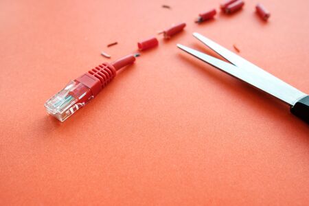 red patch cord for Internet connection on a red background is cut with scissors. damage to the cable so that there is no Internet in the houseの写真素材