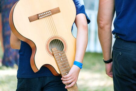 a young guitarist is walking with a guitar behind his back, and his father is walking next to him. performing at the forest festivalの写真素材