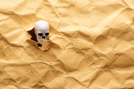 the skeleton's head sticks out through torn paper with uneven edges. sudden appearance of evilの写真素材