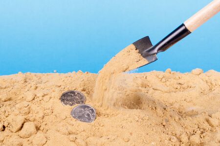 Close-up of a shovel throws sand coins over blue background. sand pour moneyの写真素材