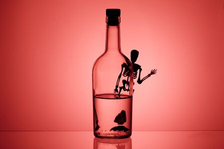 a silhouette of a skeleton peeps out from behind a bottle and waves a hand. death is near for those who are a drunkardの写真素材