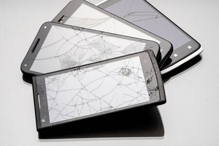 four smartphones with cracks on the screen are fan-shaped. broken phones on a gray surfaceの写真素材