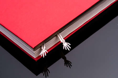 two hands of a human skeleton stick out from a closed red book. scary secrets secrets booksの写真素材