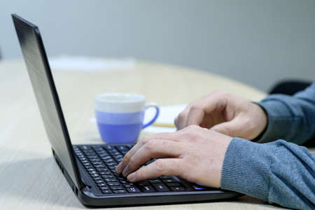 white man is typing on laptop in the background blurred mug. only hands are visible