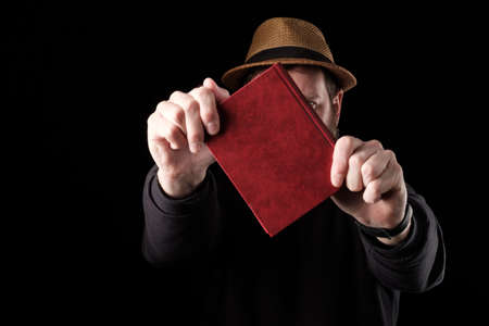 a white bearded man in a hat holds a book in front of him with both hands, defends himself like a...