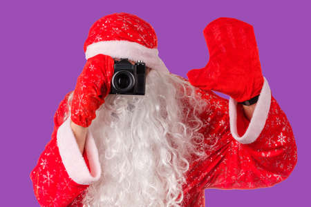santa claus takes pictures with an old camera. christmas photo lilac backgroundの写真素材
