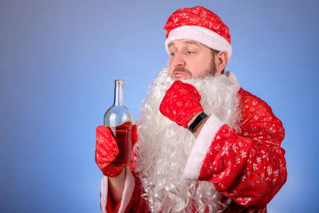 a man in a santa suit takes off his false beard to drink alcohol. drinking alcohol before the holidayの写真素材