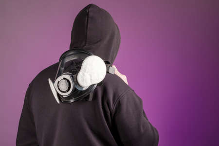 a man in a hood with a gas mask on his right shoulder turned his back to us. background purpleの写真素材