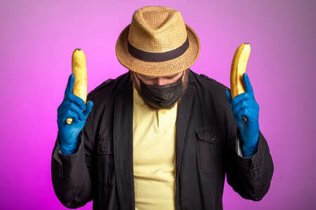 a man in a mask and a hat holds bananas in both hands as a weapon. irony about carrying arms