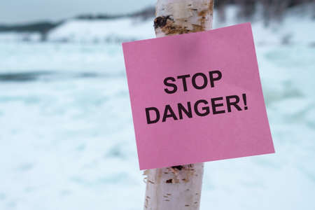stop is dangerously written on a piece of paper glued to a wooden post. homemade sign of danger of falling through the iceの写真素材