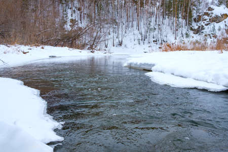 unfrozen river in the forest in winter, snow and ice on the banks. winter landscape with river