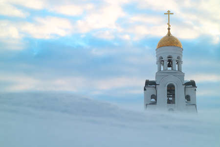 winter morning chapel and blue sky, in the foreground a blizzard on a snowy hill. winter view in...