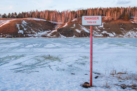 on the shore of the reservoir a sign with the inscription thin ice. danger to life