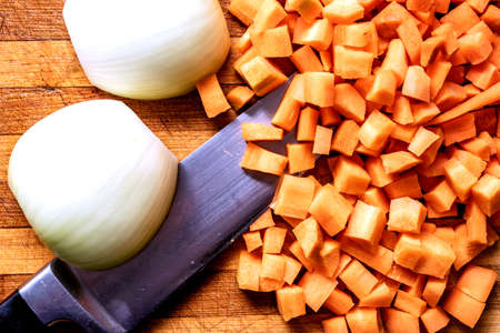 on the old wooden cutting Board are onions and a knife with carrots, all cutの写真素材