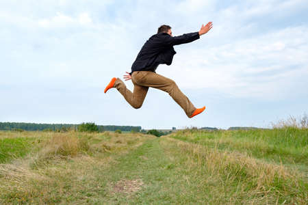 running white man at the moment of jumping with his hand forward over the field. the joy of being in nature after a long work in the cityの写真素材