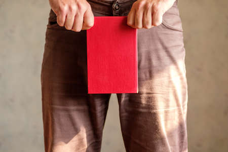 a man in clothes covers his groin with a red book holding it with both hands. book groin protectionの写真素材