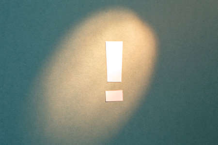 Exclamation mark cut out of paper on a textural green background highlighted by light. indicating light to actionの写真素材