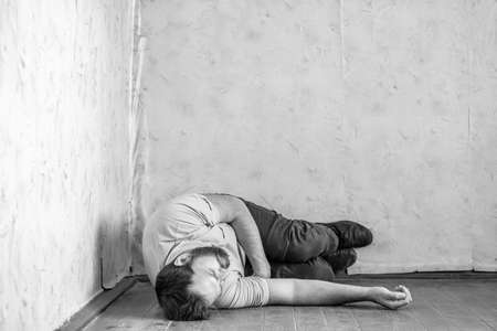 a man with a beard curled up on a dirty floor. fell asleep on the floor in the old roomの写真素材