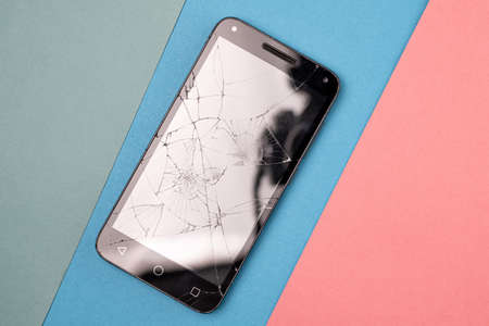 on a three-color background is a broken smartphone with broken glass, the smartphone requires screen repairの写真素材