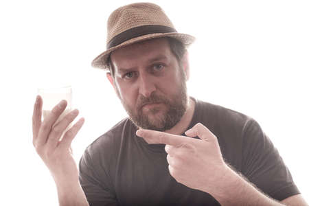 the man points to the glass of milk in his hand with the finger of his other hand. bearded man in hat on white backgroundの写真素材