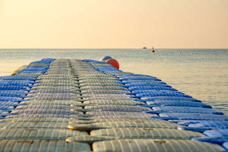 plastic pontoon on the sea going into the distance for swimming. in the background a lone ship out of focusの写真素材