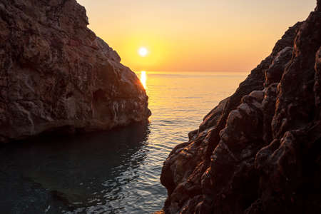 between two large stones the sun rises over the sea the glare of light on the stonesの写真素材