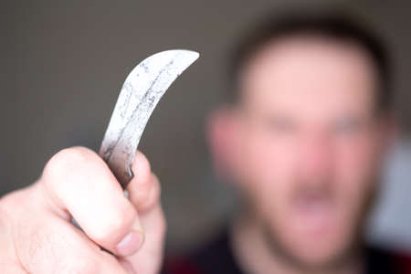 in the foreground a man's hand with a dirty folding curved knife in the background blur out of focus...