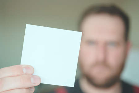 a serious man with a beard holds a clean square piece of paper in front of him. unpleasant messagesの写真素材