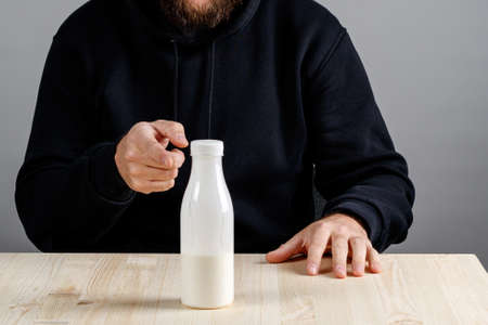 a bottle with milk on the table, a hand indicates to drink it or not to drink it. man doubts the benefits of dairy drinksの写真素材
