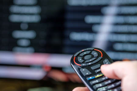 the male right hand holds the remote aimed at the TV, the background of the TV is blurred. switching...