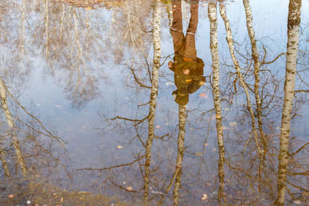 a man in a respirator with a backpack reflected in the water. spring walk in gas mask