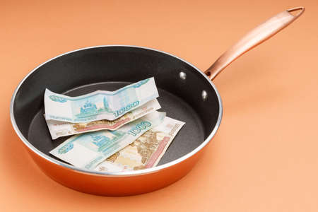 money on a large metal frying pan, orange background. debt concept, debt is growing all the time