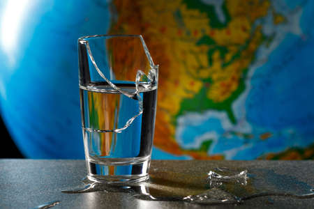 broken glass and its fragments with leaked water on the background of the globe, map of america. water problems on the planetの写真素材