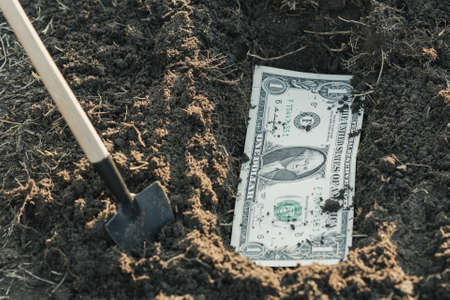a shovel near the dug hole in it a dollar, bury the money in the ground. safety of moneyの写真素材
