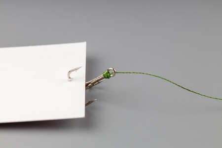 white business card on a gray background hooked with a fishing hook tied to a thread. tying and...