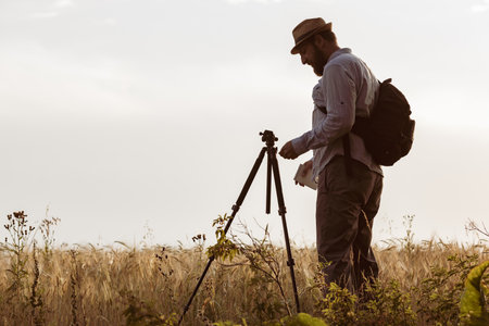 a surveyor with a beard set up a tripod on the field. man keeps records of agricultural holdingsの写真素材