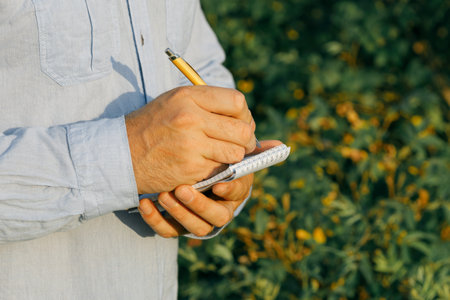 a man keeps notes in a notebook while standing in nature near a bush of berries. bush blurred out of focusの写真素材