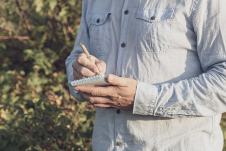 the writer writes down thoughts while standing in nature. scientist botanist taking notes
