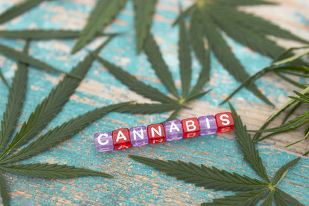 the inscription cannabis is laid out from cubes, marijuana leaves are spread around, the background is a wooden surface with peeling paintの写真素材