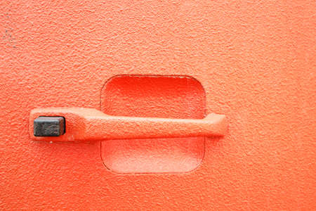 an orange handle on an old car is orange with a black button. retro car door part