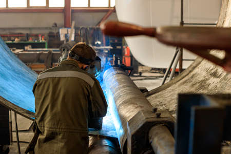 the machine in the shop near a large metal part is a welder and is doing the welding. shop floor...