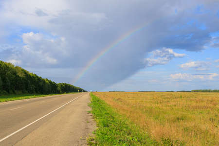 view from the side of the road and the rainbow above it. road stretching into the distance on a summer dayの写真素材
