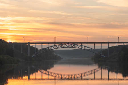 landscape of a railway bridge over the river during sunset, clouds reflecting in the riverの写真素材