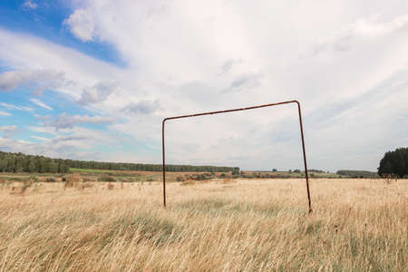 dry grass on a field with an old goal for playing football, an abandoned field overgrown with grass