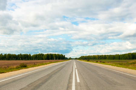 road with bad asphalt and markings leading into the forest, blue sky above the road