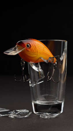 vertical photo fishing orange bait with hooks on the edge of a glass beaker. dark backgroundの写真素材