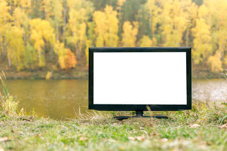 TV set on the bank of the river in autumn, on the other bank there is an autumn deciduous forest. mockup on the TV screenの写真素材