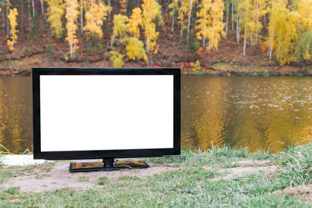 a blank TV screen that stands on the bank of the river outdoors, an autumn forest on the back pallet out of focusの写真素材